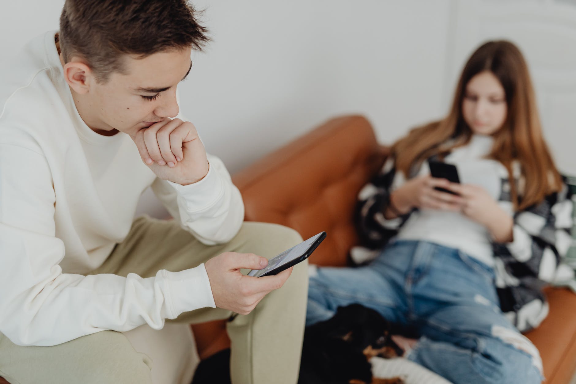teenage boy and girl sitting on a couch and using smartphones